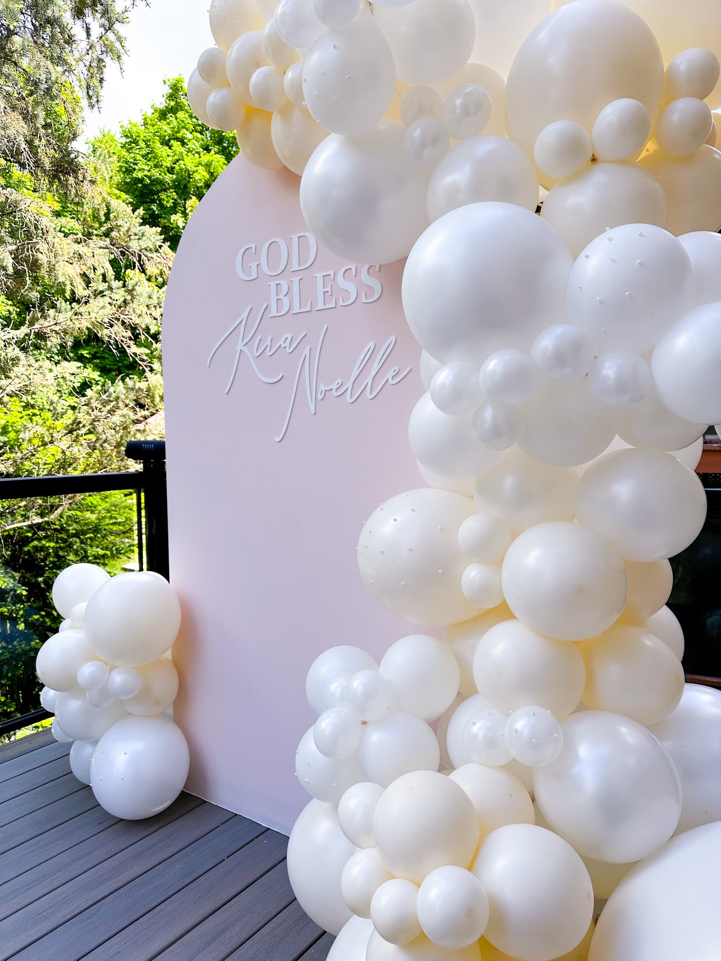 Balloon arch with 'GOD BLESS' text against a pink backdrop outdoors